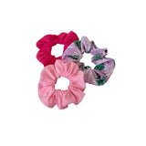 Three scrunchies, two pink and one with a leaf pattern, on a white background.