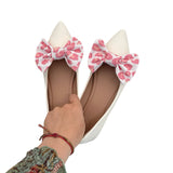 White shoes with pink leopard print bows held by a hand on a white background