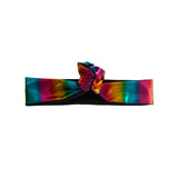 A wide black headband with a large metallic rainbow bow at the center, photographed on a plain white background.