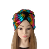 A metallic rainbow holographic knotted headwrap turban hat displayed on a mannequin head with long light brown hair against a plain white background.