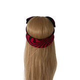A long blonde wig with a red and black wavy patterned headband, shown from the back on a mannequin head against a white background.
