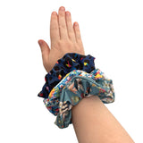Hand wearing a colorful scrunchie with three additional scrunchies stacked on top, on a white background.