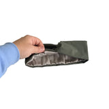 A hand wearing a light blue long-sleeve shirt holds open a dark olive green pouch or sleeve, showing a shiny silver-gray satin lining, against a plain white background.