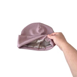 Pink ribbed baby hat held by a hand on a white background