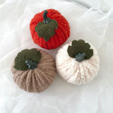 three sherpa pumpkins in red, white, brown, and beige on a white fabric background.