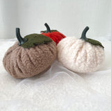 Three boucle pumpkins in brown, red, and white on a textured white surface.