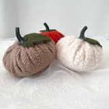 Three boucle pumpkins in brown, red, and white on a textured white surface.