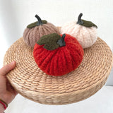 Three knitted pumpkins in red, beige, and brown on a woven surface.