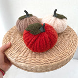 Three knitted pumpkins in red, beige, and brown on a woven surface.