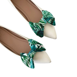 White pointed-toe shoes with green leaf-patterned shoe clips on a white background