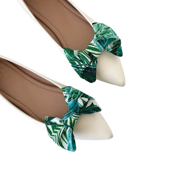 White pointed-toe shoes with green leaf-patterned shoe clips on a white background
