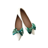 White pointed-toe shoes with green leaf-patterned bows on a white background