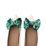 White shoes with green leaf-patterned bows on a white background