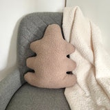 Oak leaf-shaped pillow with textured surface on a gray chair next to a white blanket