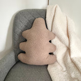 Oak leaf-shaped pillow with textured surface on a gray chair next to a white blanket