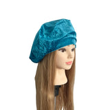 Mannequin head with long brown hair wearing a blue velvet beret on a white background