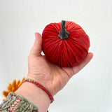 Hand holding a red fabric pumpkin against a white background