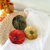 Three colorful velvet pumpkins on a woven mat with a white fabric background