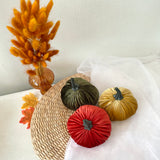 Decorative pumpkins in red, green, and gold on a woven surface with dried orange grasses.