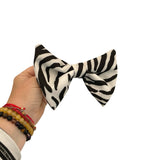 Hand holding a zebra print bow with bracelets on a white background