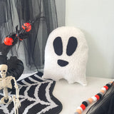 Decorative ghost pillow with black eyes and mouth on a Halloween-themed setting with skeleton, spider webs, and candy.
