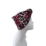 A red, black, and white leopard print headband styled on a white mannequin head in profile against a solid white background.
