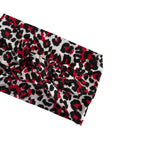 A textured fabric headband with a red, black, and white leopard print pattern, folded diagonally on a plain white background.