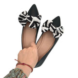 Black flats with zebra print bows held by a hand on a white background