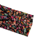 A black fabric headband featuring an all-over print of colorful autumn leaves in shades of pink, orange, green, and red, styled with a large knot on the side, shown against a plain white background.