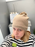 Person wearing a beige beanie with a pom-pom, sitting in front of a sewing machine.