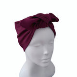 A deep burgundy ribbed fabric headwrap turban with a large bow, displayed on a white mannequin head against a plain white background.