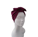 A deep burgundy ribbed fabric headwrap turban with a large twisted knot, displayed on a white mannequin head against a plain white background.