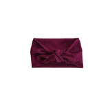 A ribbed fabric headband in deep burgundy, styled with a large bow at the center front, shown flat against a solid white background.