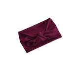 A deep burgundy ribbed fabric headband with a large bow knot, shown on a plain white background.