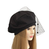Black velvet hat with a netting veil on a mannequin head against a white background