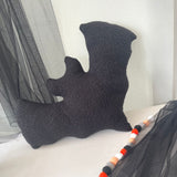 Black textured pillow on a bed with striped curtains in the background