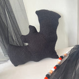 Black textured pillow on a bed with striped curtains in the background