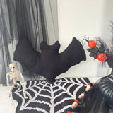 Halloween-themed decor with a black knitted bat, skeleton, and pumpkins on a spiderweb rug.