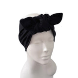 A black velvet turban headband with a large bow, displayed on a light gray mannequin head against a plain white background.