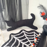Black cat cushion  on a white surface with a spider web decoration and feathers in the background.