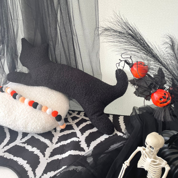 Halloween-themed decor with a black cat, skeleton, and pumpkins on a spiderweb rug.