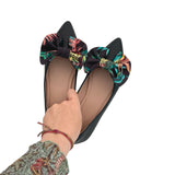 Black flats with floral bows worn by a person on a white background