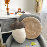 Round woven pillow and acorn-shaped cushion on a gray chair with decorative items in the background.
