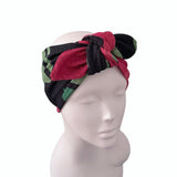 A multicolor patterned headwrap turban hat with a large bow, displayed on a white mannequin head against a plain white background.