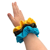 Hand wearing three colorful scrunchies on a white background