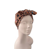 A leopard print hair wrap headband with a large bow, displayed on a neutral mannequin head against a solid white background.