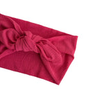 A close-up of a textured, deep pink fabric headband with a knotted bow detail, shown against a plain white background.