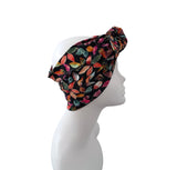 A multicolor leaf-patterned headwrap turban hat displayed on a white mannequin head against a solid white background.