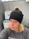 Person wearing a black beanie with a fluffy pom-pom, standing indoors.