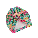 A knotted fabric headband featuring a colorful floral print with pink, yellow, and peach flowers on a mint green background, with a sheer white lining visible at the bottom.